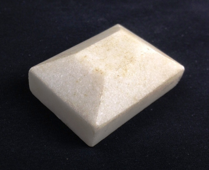 A square piece of white soap sitting on a black surface.