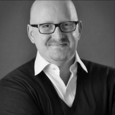 A black and white photo of a bald man with glasses.