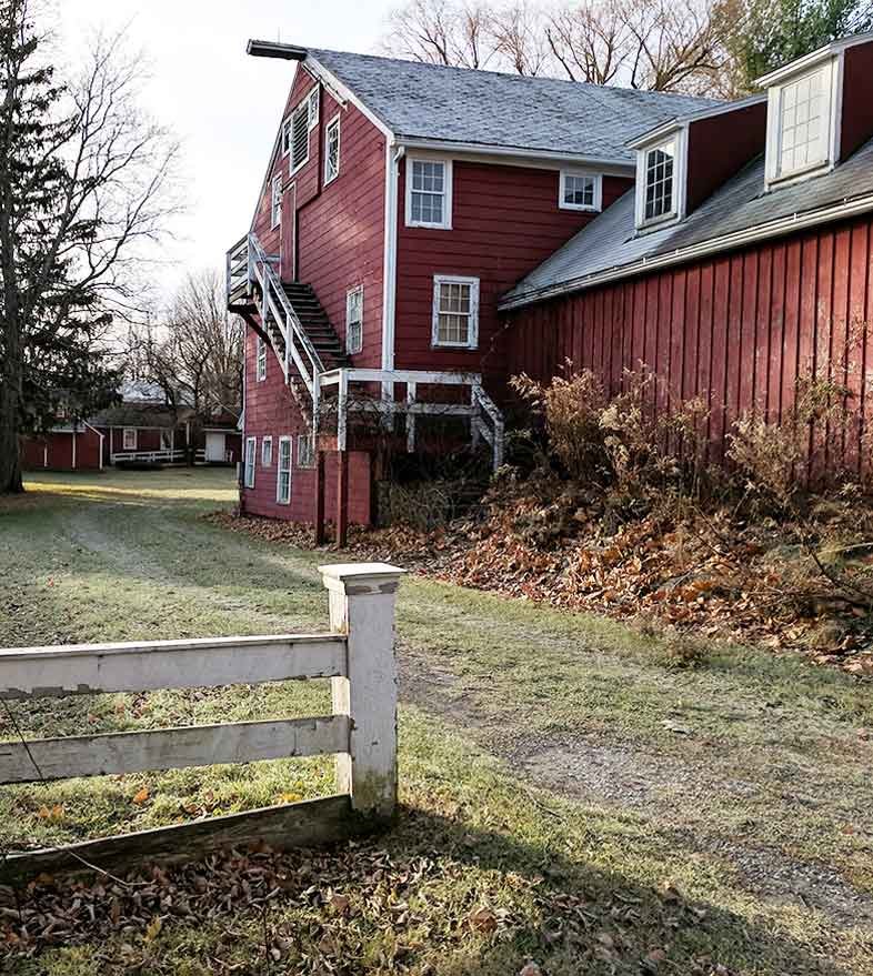 A red barn with a white fence in front of it.