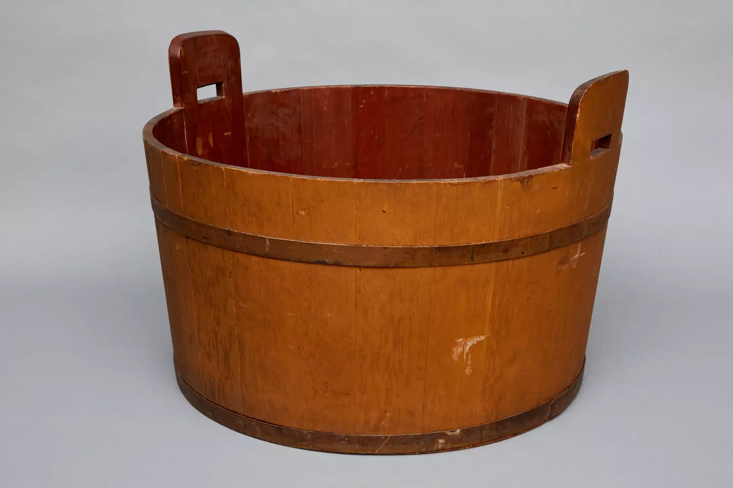 A wooden bucket with handles on a gray background.