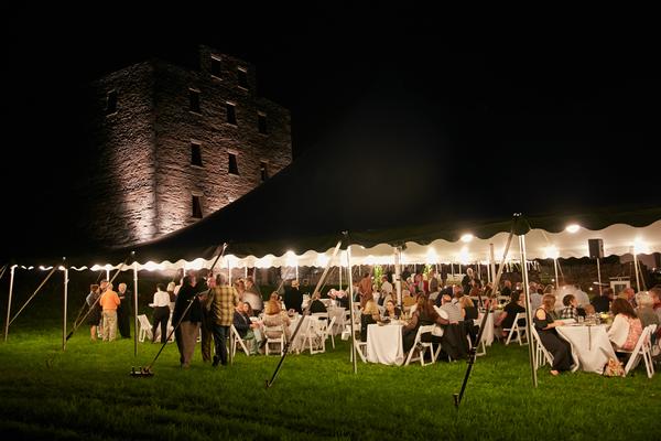 A wedding reception under a tent at night with a castle in the background.