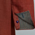A close up of a red blazer with a blue button.