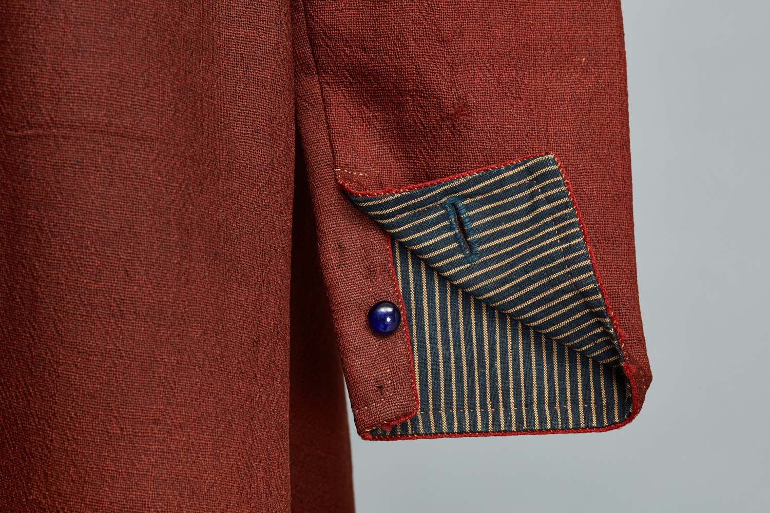 A close up of a red blazer with a blue button.