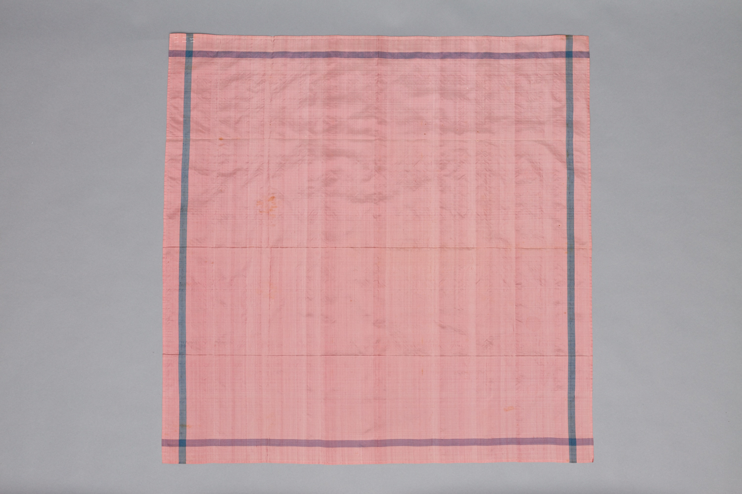 A pink and blue cloth hanging on a gray background.