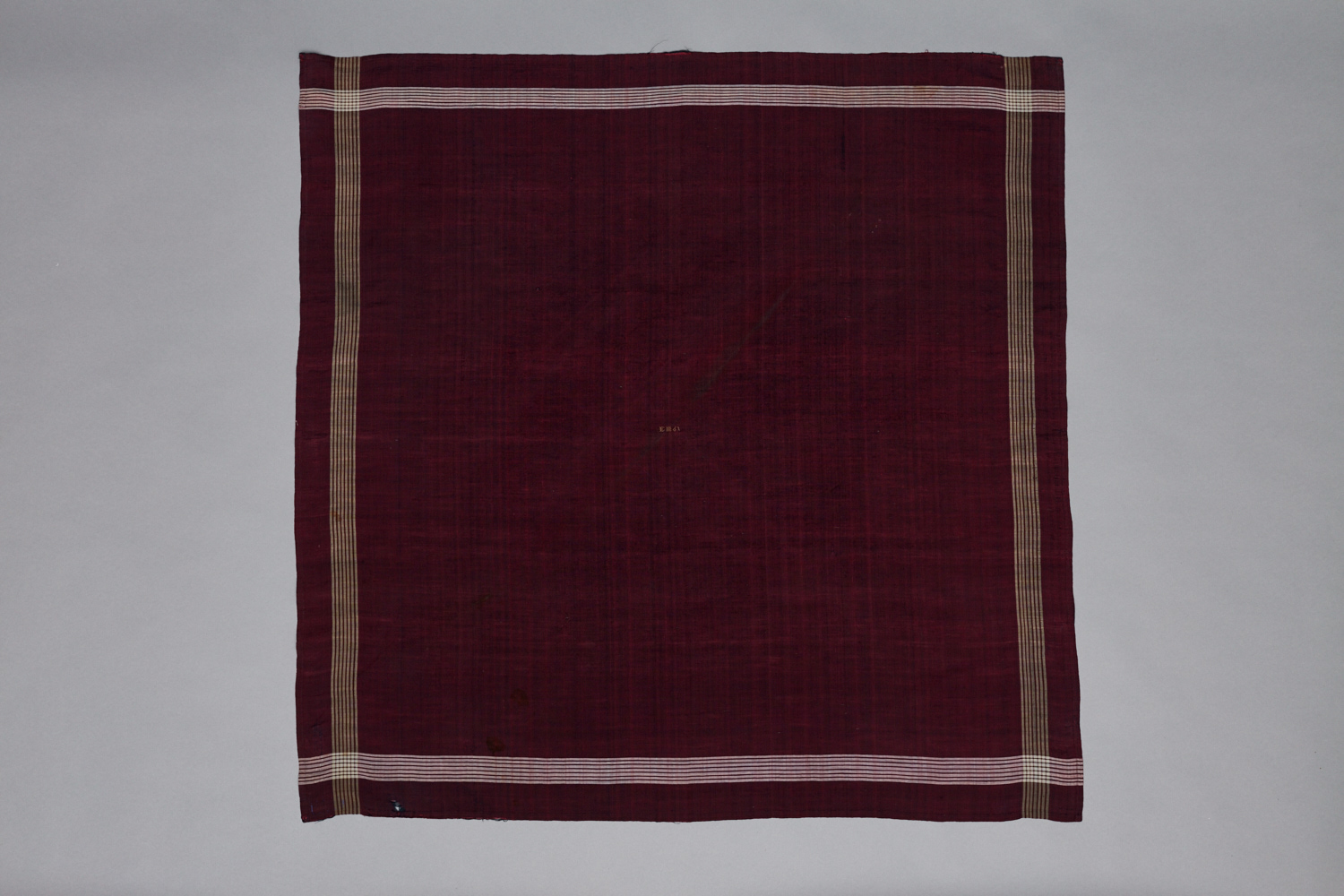 A maroon and tan striped cloth hanging on a gray background.