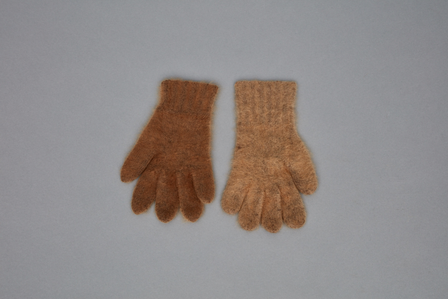 A pair of brown wool gloves on a gray surface.