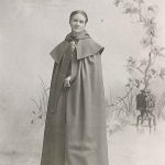 An old photo of a woman in a cloak.