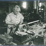 An old black and white photo of a woman working in a workshop.