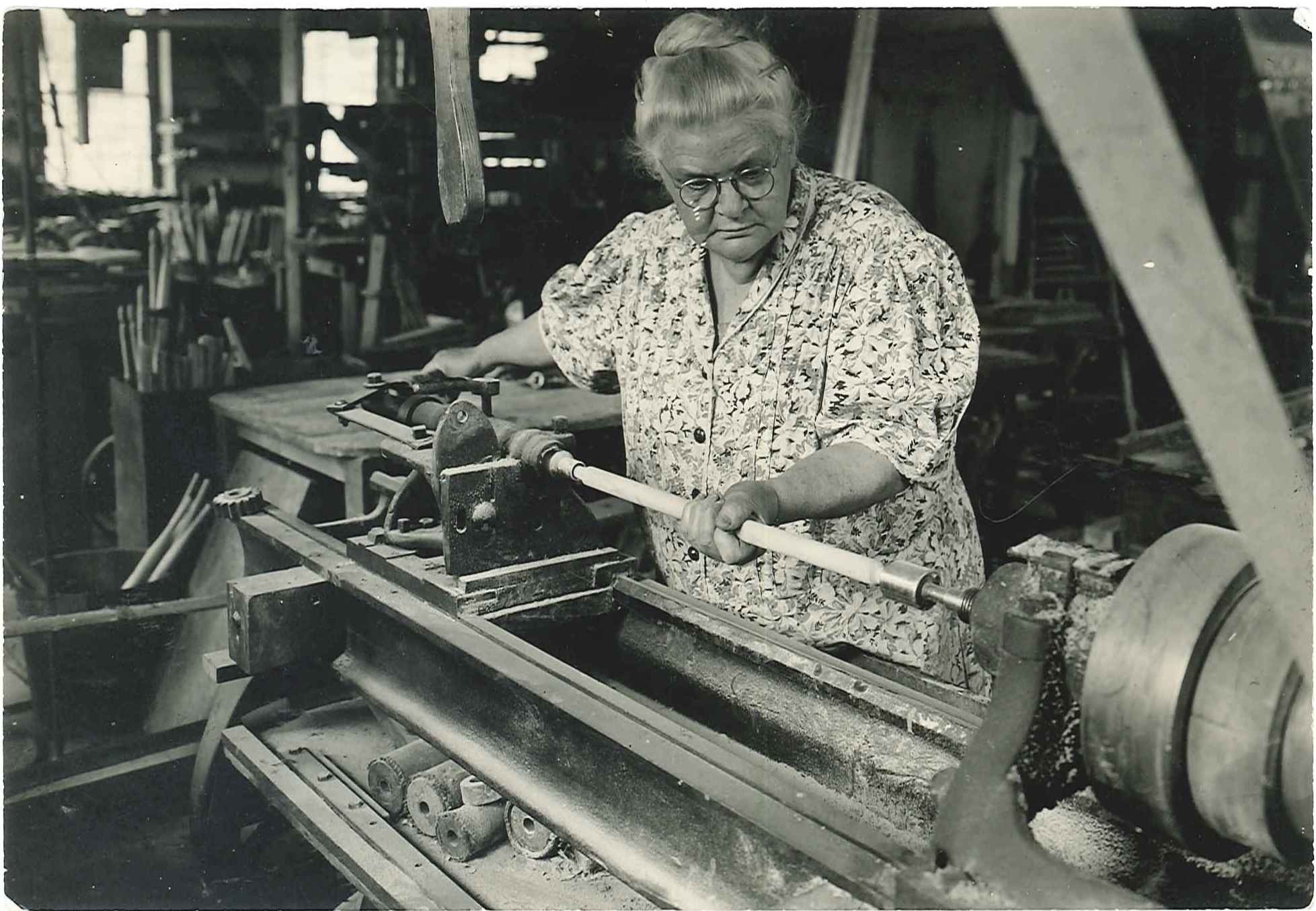 An old black and white photo of a woman working on a lathe.