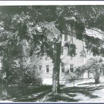 A black and white photo of a house with trees.