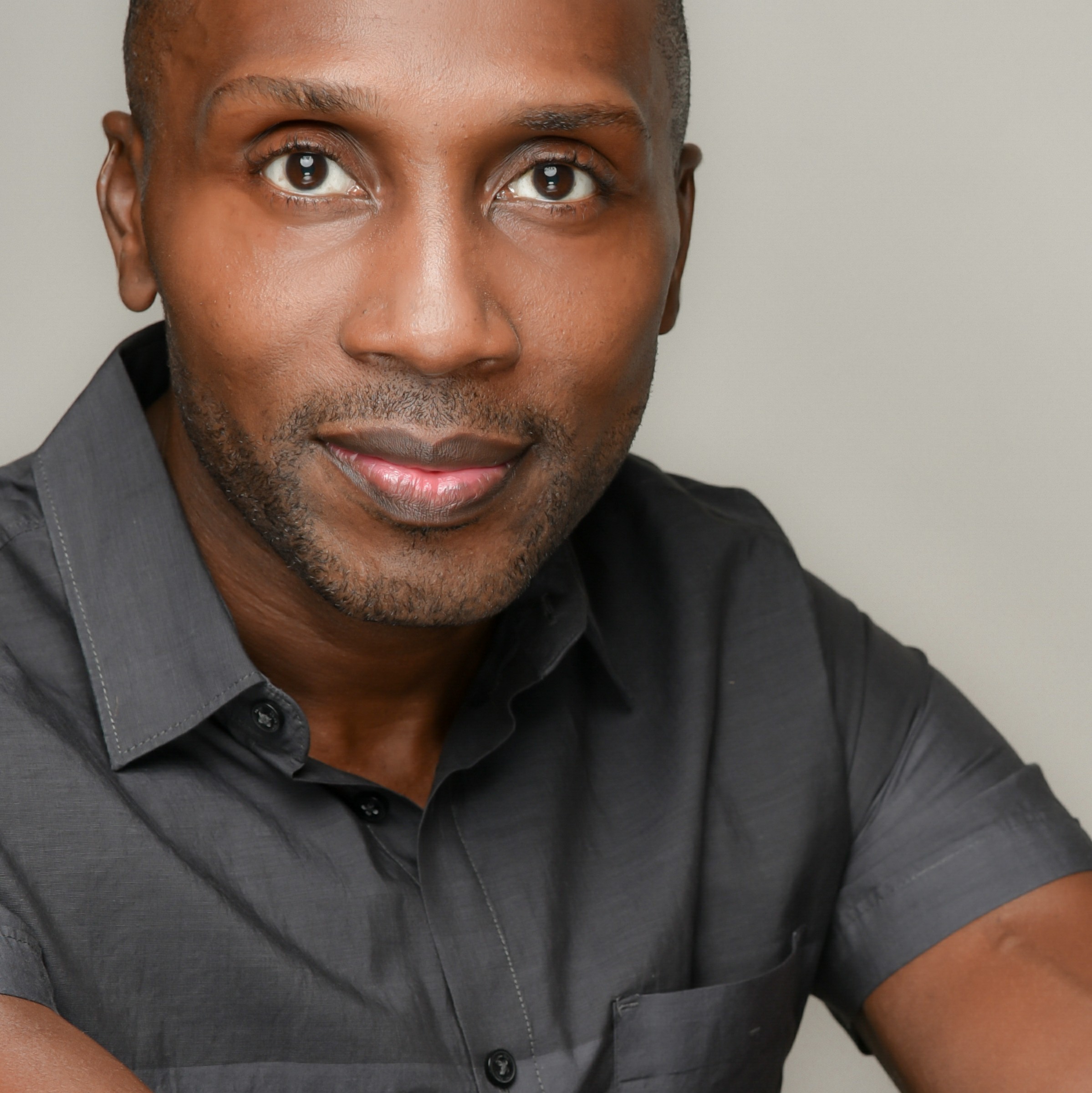 A black man in a gray shirt is posing for a photo.