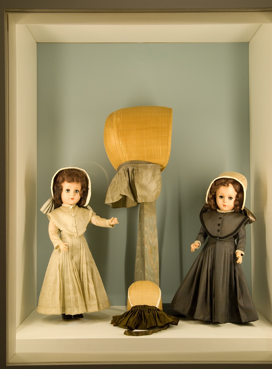 Three dolls with hats in a display case.