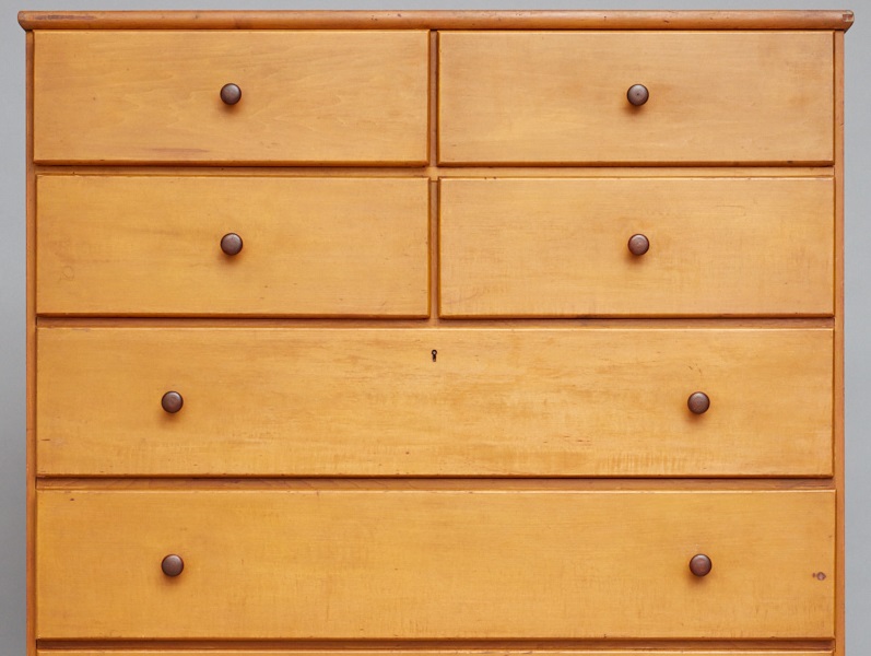 A wooden chest of drawers is shown against a gray background.