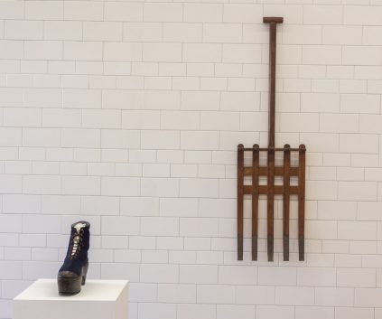 A wooden rake and a pair of shoes on a white wall.