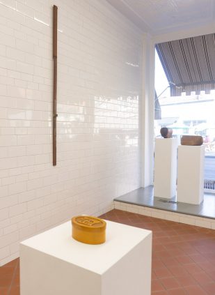 A room with a yellow vase on a white pedestal.