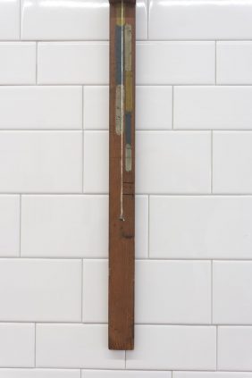 A wooden thermometer hanging on a tiled wall.