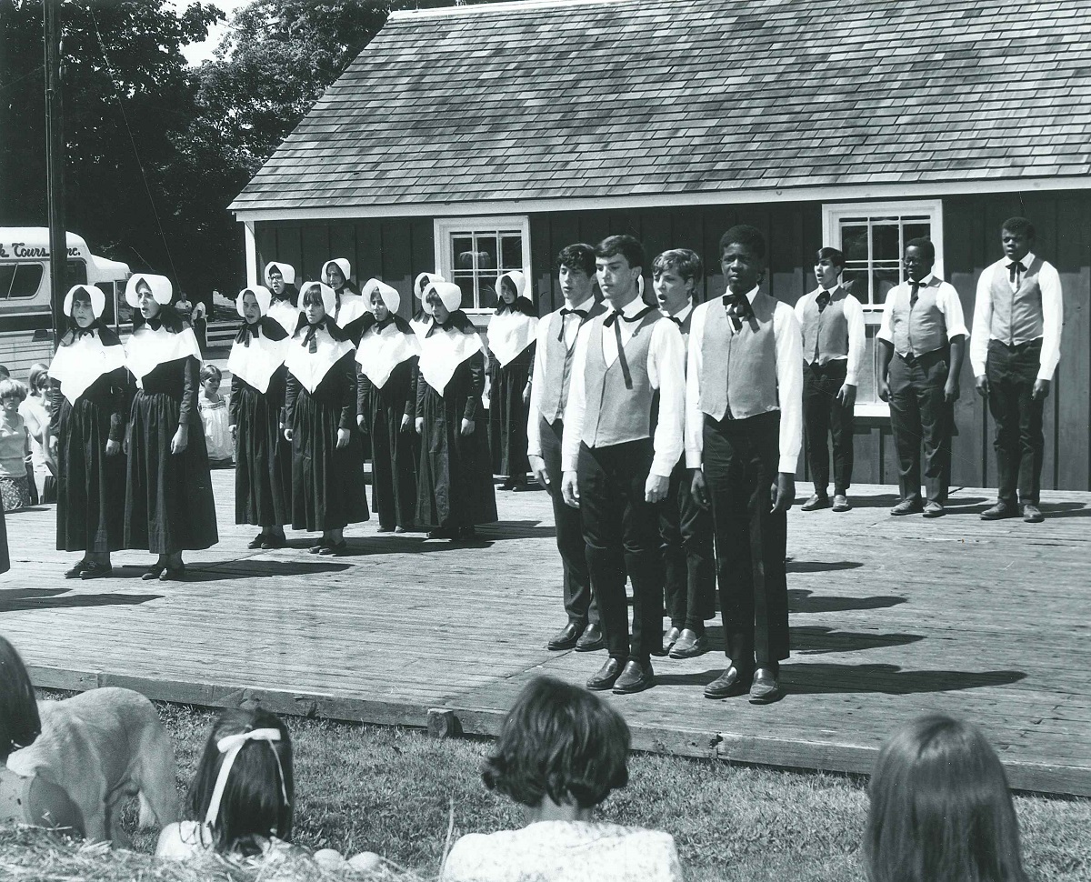 A black and white photo of a group of people standing in front of a house.