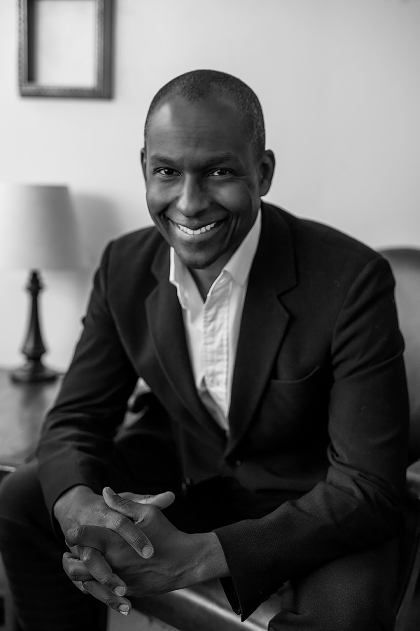 A black and white photo of a smiling man in a suit.