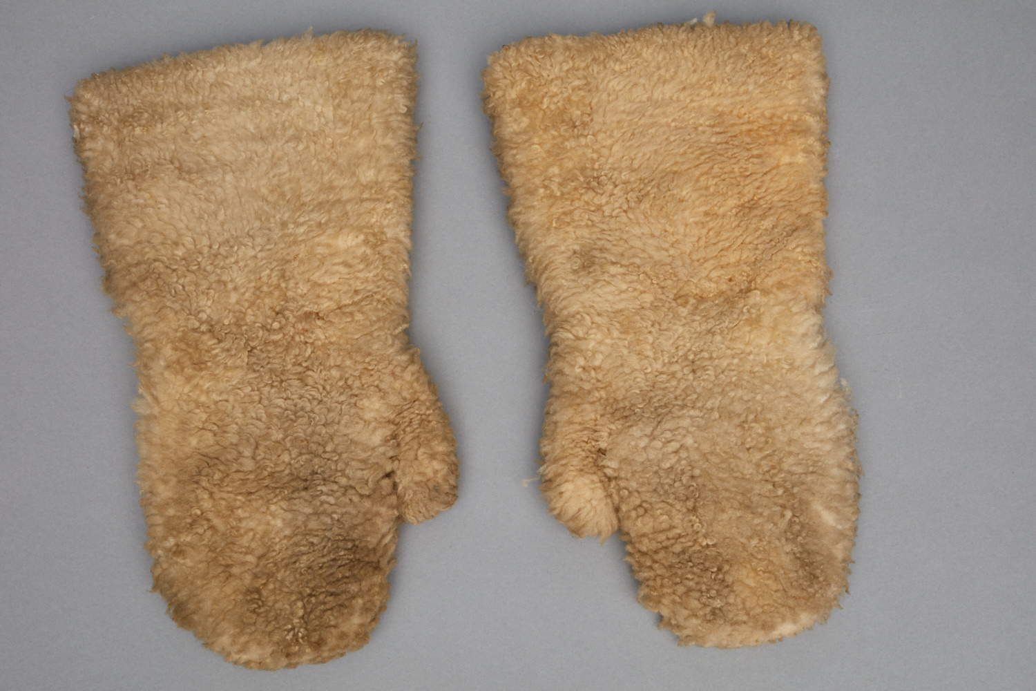 A pair of beige mittens on a gray surface.