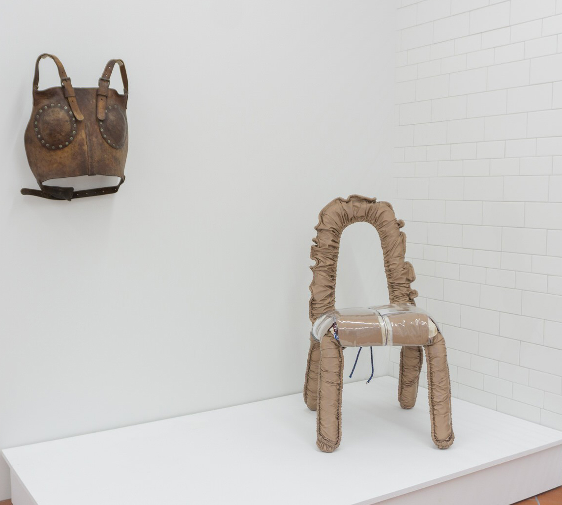 A chair and a bag on display in a white room.