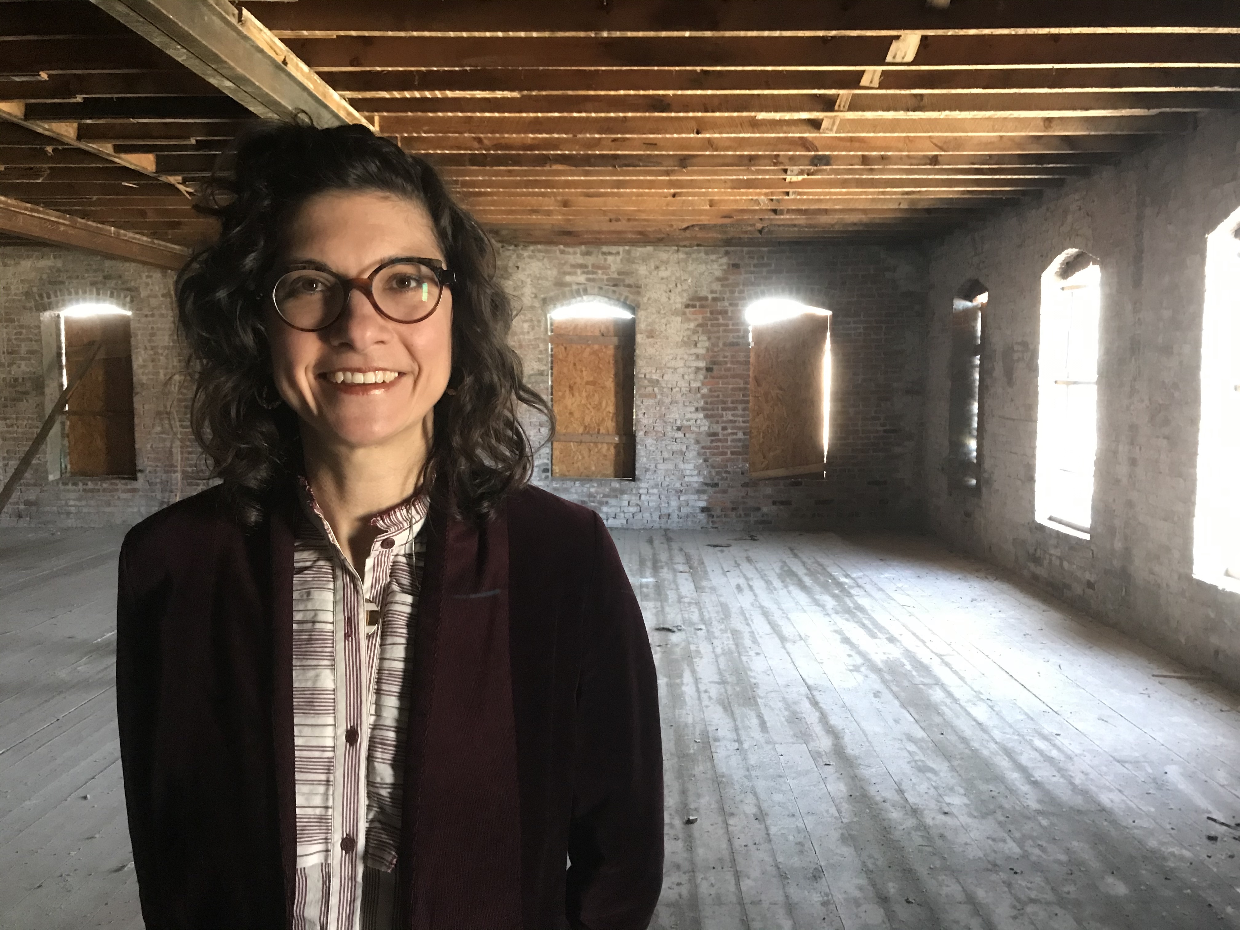 A woman in glasses standing in an empty room.