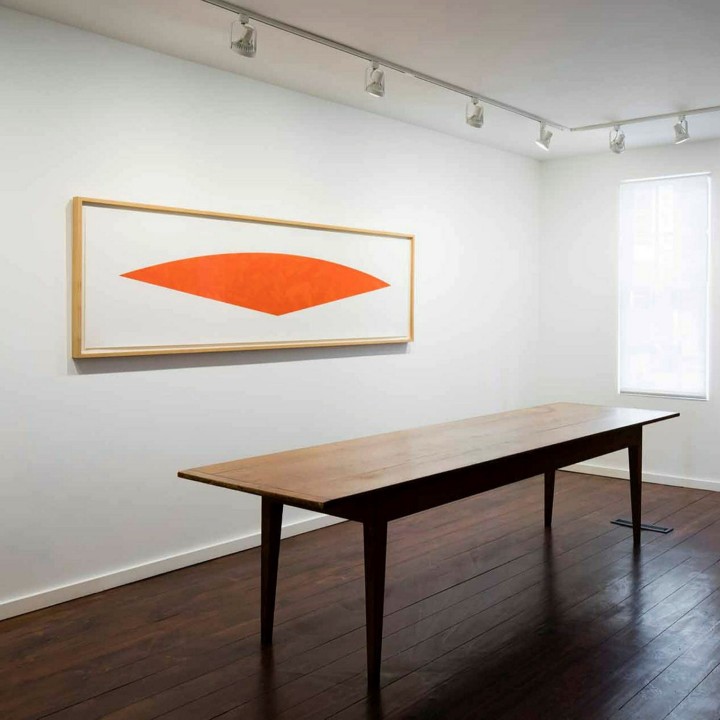 An orange painting hangs above a wooden table in an empty room.