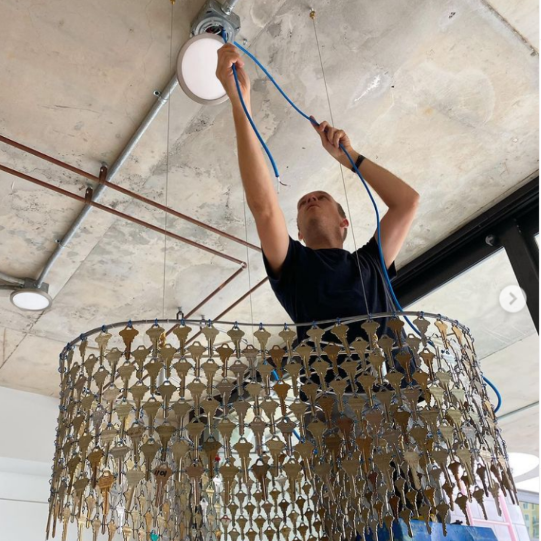 A man is hanging a large metal chandelier in an office.