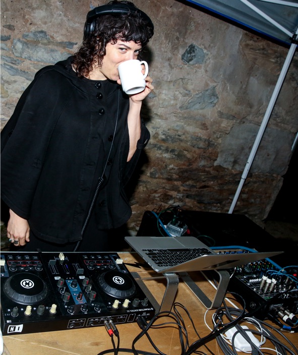 A woman drinking a cup of coffee in front of a dj set.