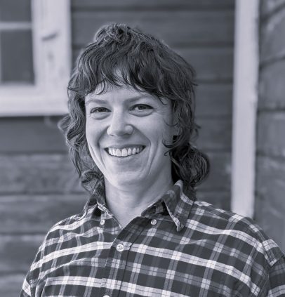 A black and white photo of a smiling woman in a plaid shirt.