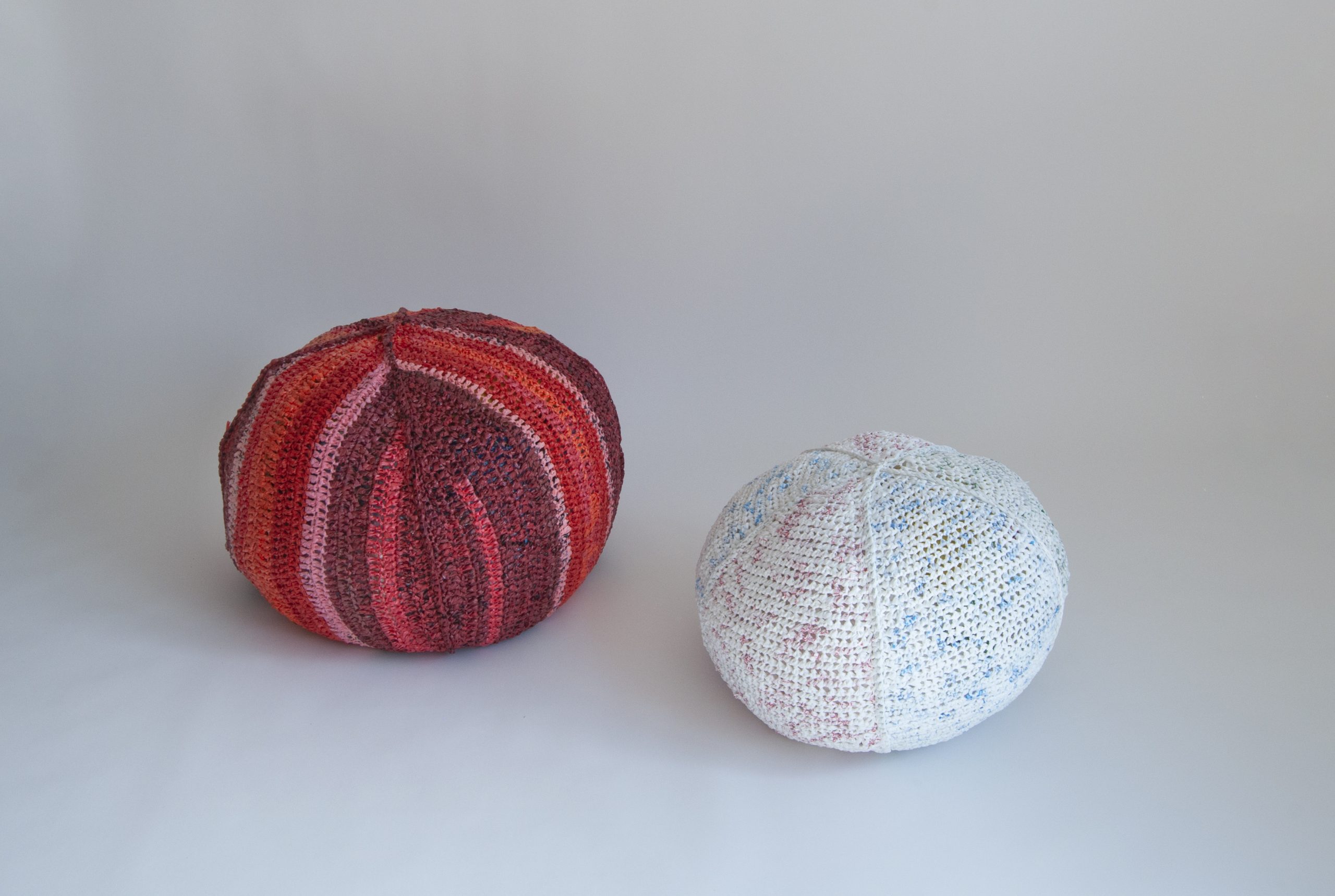 Two knitted poufs made of plarn on a white surface.