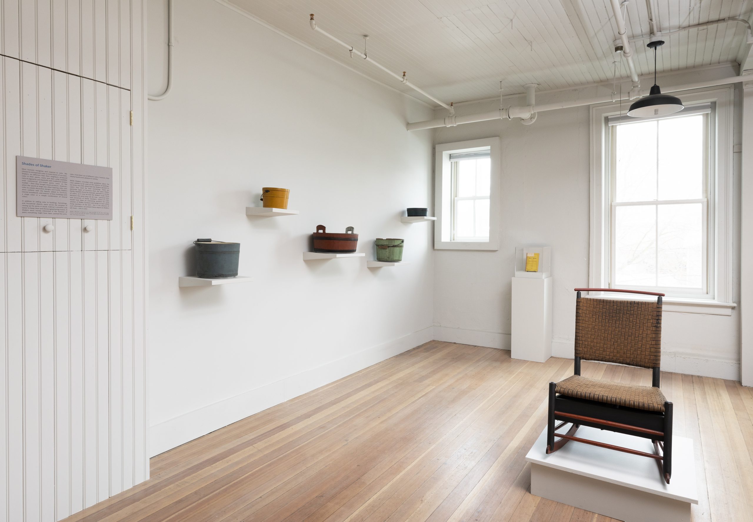 Minimalist art gallery interior with pottery displayed on wall shelves and a single chair in the foreground.