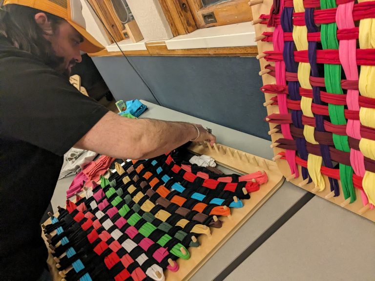 A person weaving colorful fabric strips on a loom.