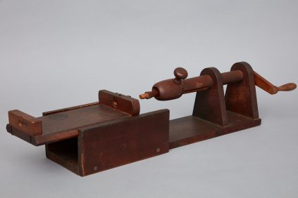 A vintage wooden mechanical device with a handle and clamps, likely an old lathe or tool for shaping or holding objects.