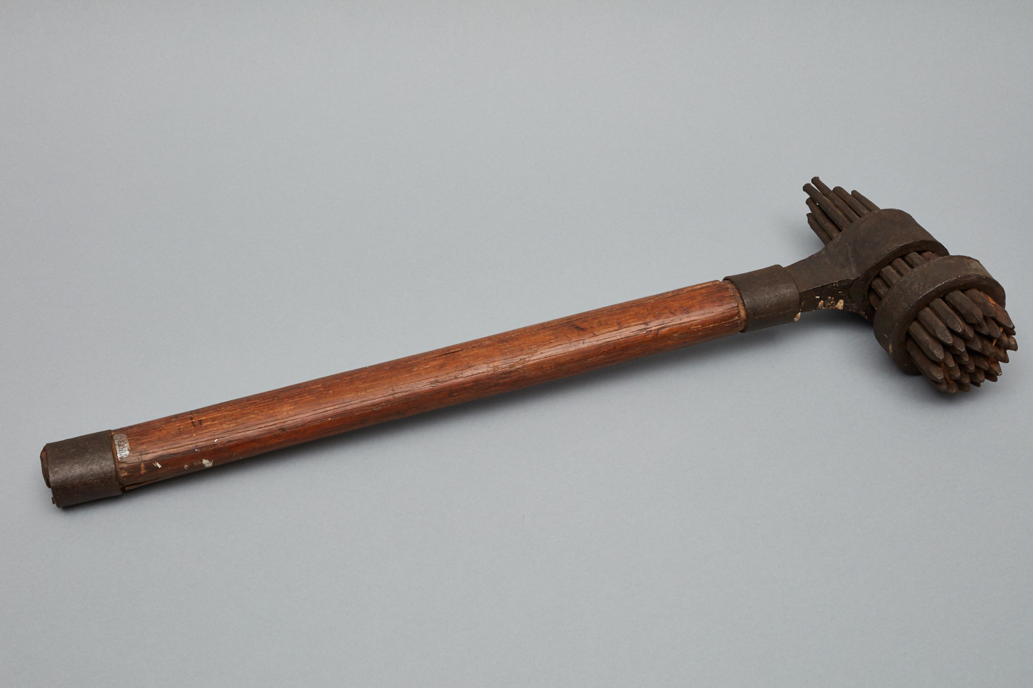 A vintage wooden mallet with a cylindrical metal head featuring clustered metal spikes.